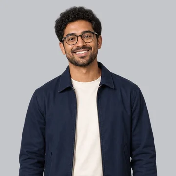 Guest photo: a smiling person with curly dark hair and glasses in a navy jacket